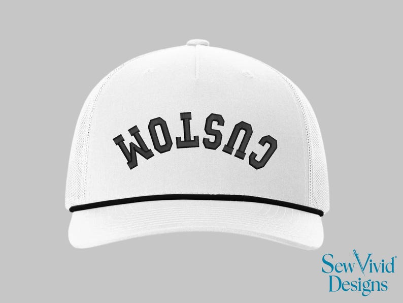 May include: White trucker hat with the word "CUSTOM" embroidered in black block letters. The hat has a black rope detail and a mesh back. The Sew Vivid Designs logo is in the bottom right corner.