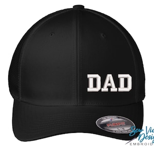 May include: Black baseball cap with the word "DAD" embroidered in white block letters. The cap has a curved brim and a mesh back for breathability. The cap is a Flexfit brand.