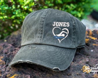 May include: A black distressed baseball cap with a white heart and a swimmer graphic. The text "JONES" is embroidered on the cap.