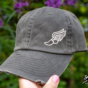 May include: A gray distressed baseball cap with a white embroidered winged foot design. The cap has a slightly curved brim and a distressed look.