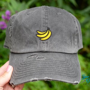 May include: A gray distressed baseball cap with a yellow banana graphic embroidered on the front.