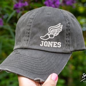 May include: A gray distressed baseball cap with a white embroidered winged foot and the name "JONES" underneath.