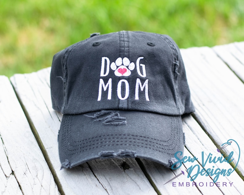 Pode incluir: Um bon&eacute; de beisebol preto desgastado com bordado branco que diz "Dog Mom" com um cora&ccedil;&atilde;o vermelho dentro de uma pegada de pata.