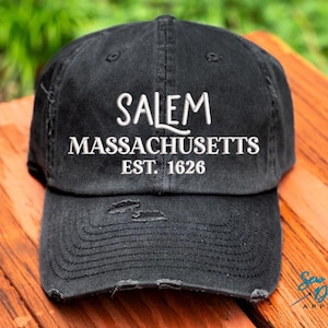 May include: Black distressed baseball cap with white embroidered text that reads "Salem Massachusetts Est. 1626".