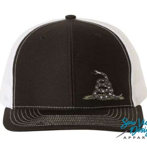 May include: A black and white trucker hat with a white mesh back. The hat features an embroidered image of a coiled snake with a 'Don't Tread On Me' design.