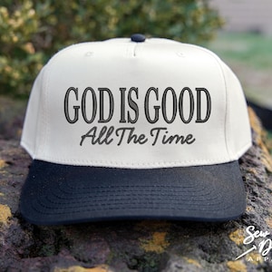 K&ouml;nnte beinhalten: Eine Baseballkappe mit f&uuml;nf Paneelen, einer cremefarbenen Krone und einem einfarbigen schwarzen Schirm. Auf der Vorderseite der Krone befindet sich eine schwarze Stickerei mit dem Text GOD IS GOOD in fetter Serifenschrift und All The Time darunter.