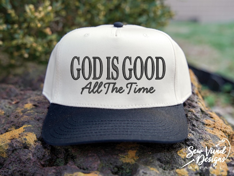 K&ouml;nnte beinhalten: Eine Baseballkappe mit f&uuml;nf Paneelen, einer cremefarbenen Krone und einem einfarbigen schwarzen Schirm. Auf der Vorderseite der Krone befindet sich eine schwarze Stickerei mit dem Text GOD IS GOOD in fetter Serifenschrift und All The Time darunter.