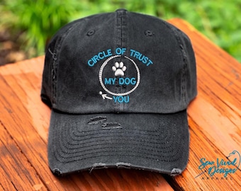May include: Black distressed baseball cap with blue embroidery that reads "Circle of Trust My Dog You" with a paw print inside the circle.