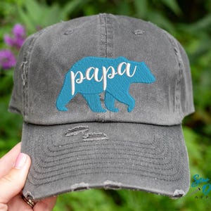 May include: A gray distressed baseball cap with a blue bear silhouette and the word "papa" embroidered in white.