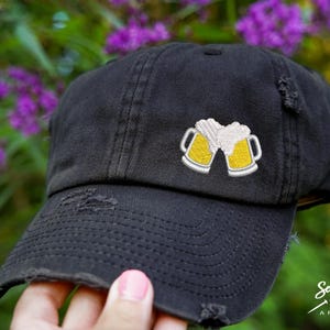May include: A black distressed baseball cap with an embroidered design of two yellow beer mugs with white foam.
