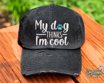 May include: Black distressed baseball cap with white embroidery that reads "My dog thinks I'm cool" with a blue paw print.