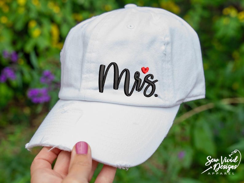 K&ouml;nnte beinhalten: Wei&szlig;e Baseballkappe mit dem in Schwarz gestickten Wort "Mrs." und einem kleinen roten Herzen &uuml;ber dem "s".