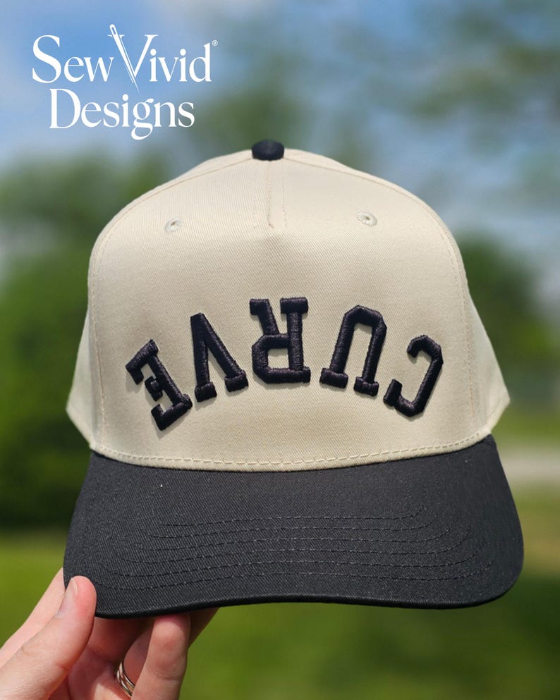 May include: A beige baseball cap with a black brim and a black button on top. The front of the cap features the word CURVE embroidered in black, bold, capital letters, positioned upside down. The text SewVivid Designs appears in the top left corner.