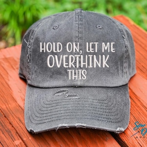 May include: A gray distressed baseball cap with the text "Hold on, let me overthink this" embroidered in white.