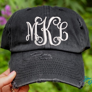 May include: A black distressed baseball cap with a white embroidered monogram "MKL" on the front.