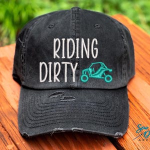 May include: Black distressed baseball cap with white embroidery that reads "Riding Dirty" and a turquoise graphic of a side-by-side vehicle.