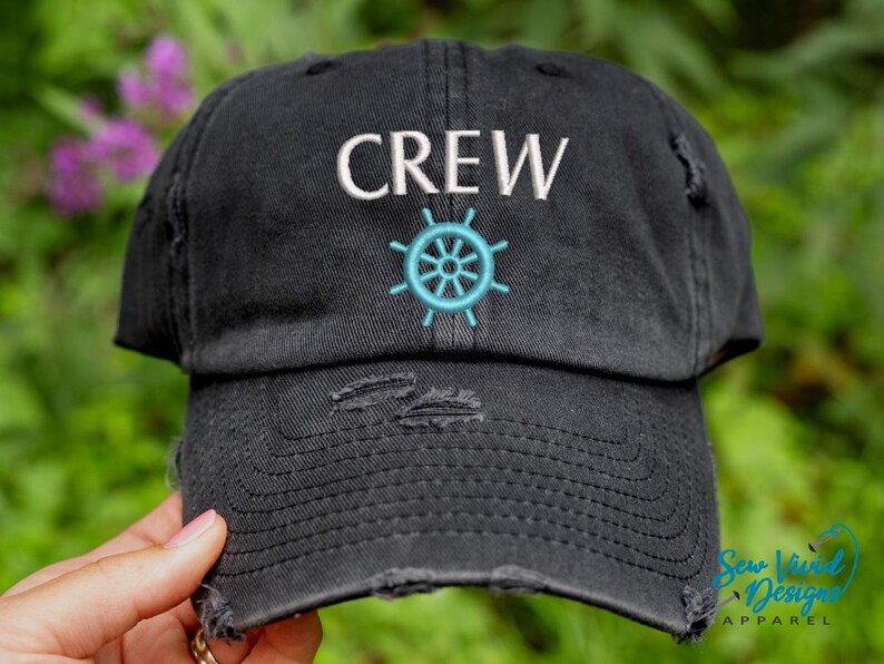 K&ouml;nnte beinhalten: Schwarze, ausgewaschene Baseballkappe mit dem Wort "CREW" in Wei&szlig; &uuml;ber einem t&uuml;rkisfarbenen Steuerraddesign gestickt. Die Kappe hat einen Used-Look mit ausgefransten Details.
