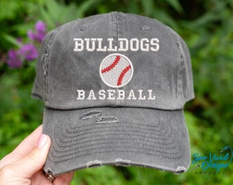 May include: A gray distressed baseball cap with white embroidery that reads "Bulldogs Baseball" and a white baseball with red stitching.