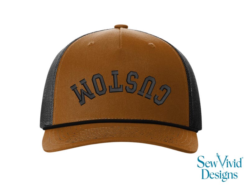 May include: A brown trucker hat with a black mesh back and a curved brim. The word "CUSTOM" is embroidered in gray block letters across the front. The hat has a snap closure and a brown button on top.