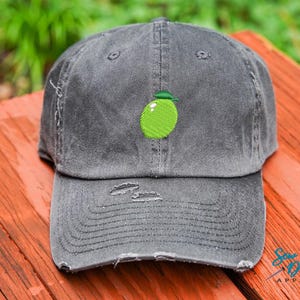 May include: A gray distressed baseball cap with a lime green embroidered lime on the front. The cap has a curved brim and a distressed look.