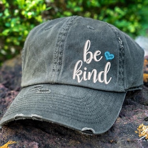 May include: A black distressed baseball cap with the phrase "be kind" embroidered in white with a blue heart.