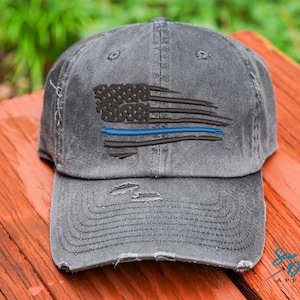 May include: A distressed black baseball cap with a thin blue line American flag design. The cap has a frayed brim and a distressed look.