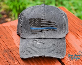 May include: A distressed black baseball cap with a thin blue line American flag design. The cap has a frayed brim and a distressed look.