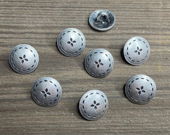 Op de afbeelding: Acht zilveren metalen knopen met een vierpuntige stervorm en een gestikte rand.