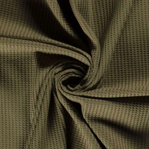 May include: Close-up of a textured, olive green waffle knit fabric. The fabric is folded and twisted, showing the texture and drape of the material.