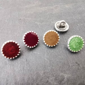 Peut inclure: Quatre boutons ronds avec un bord argenté et une bordure décorative. Les boutons sont de couleur rouge, marron, vert et bordeaux.