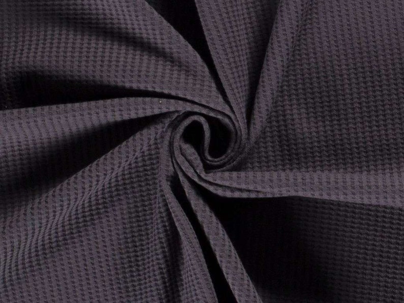 May include: A close-up of a dark purple waffle weave fabric. The fabric is folded and textured, showing the waffle pattern.