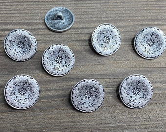 May include: Seven silver buttons with a white mandala design. The buttons are round and have a raised edge.