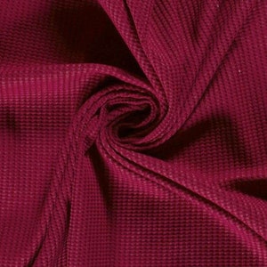 May include: Close-up of a burgundy waffle knit fabric. The fabric is soft and textured, with a subtle sheen.