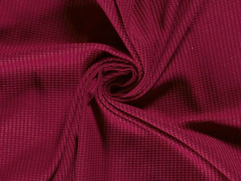 May include: Close-up of a burgundy waffle knit fabric. The fabric is soft and textured, with a subtle sheen.