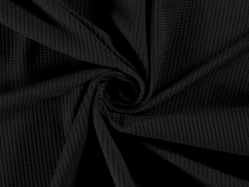 May include: Black waffle knit fabric with a textured surface. The fabric is folded and twisted, creating a swirling pattern.
