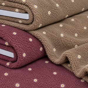 Peut inclure: Deux pièces de tissu polaire texturé pliées, l'une de couleur marron foncé et l'autre dans une teinte brun clair. Les deux pièces présentent un motif répétitif de petites fleurs de marguerite blanches avec des cœurs jaunes dispersés.