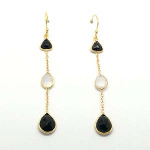 Puede incluir: Pendientes de aro dorados con gotas de piedras preciosas negras y blancas. Los pendientes presentan una piedra preciosa negra de forma triangular en la parte superior, seguida de una piedra preciosa blanca en forma de lágrima y una piedra preciosa negra en forma de lágrima en la parte inferior.