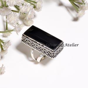 May include: A rectangular black onyx gemstone ring set in a silver band with intricate filigree scrollwork and beaded edges. The side of the silver setting features the text Silver925Atelier. The ring has a split shank design with a polished finish.