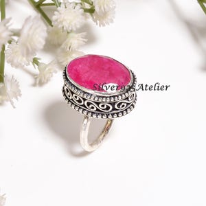 Könnte beinhalten: Ein Silberring mit einem großen, ovalen, facettierten, pinkfarbenen Edelstein, der in eine dekorative Ringschiene mit komplizierten Schnörkeln und perlenartigen Kanten gefasst ist. Der Text Silver925 Atelier ist an der Seite der Fassung sichtbar.
