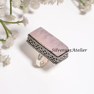 May include: A rectangular rose quartz gemstone ring set in a silver band with intricate scrollwork and beaded detailing along the edges. The inner band is stamped with 925, and the text Silver925Atelier is visible on the right side of the ring.