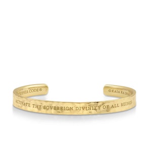 Puede incluir: Pulsera de metal martillado dorado con la inscripción "Activate the Sovereign Divinity of All Beings" y los textos "Sophia Code" y "Kaija Ra 2016".
