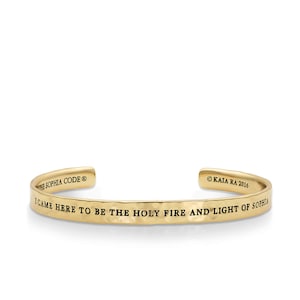 Puede incluir: Pulsera de brazalete de metal dorado con la inscripción "Vine aquí para ser el fuego sagrado y la luz de Sophia" y el texto "The Sophia Code" y "©KAIA RA 2016".
