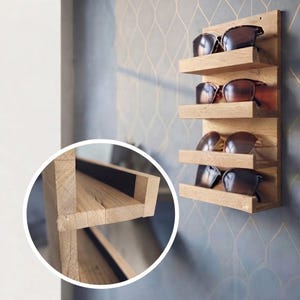 Puede incluir: Un estante de madera montado en la pared con cuatro repisas horizontales dise&ntilde;adas para guardar gafas. La veta de la madera clara es visible en toda la estructura. Un recuadro circular ofrece una vista detallada de la construcci&oacute;n y las uniones.