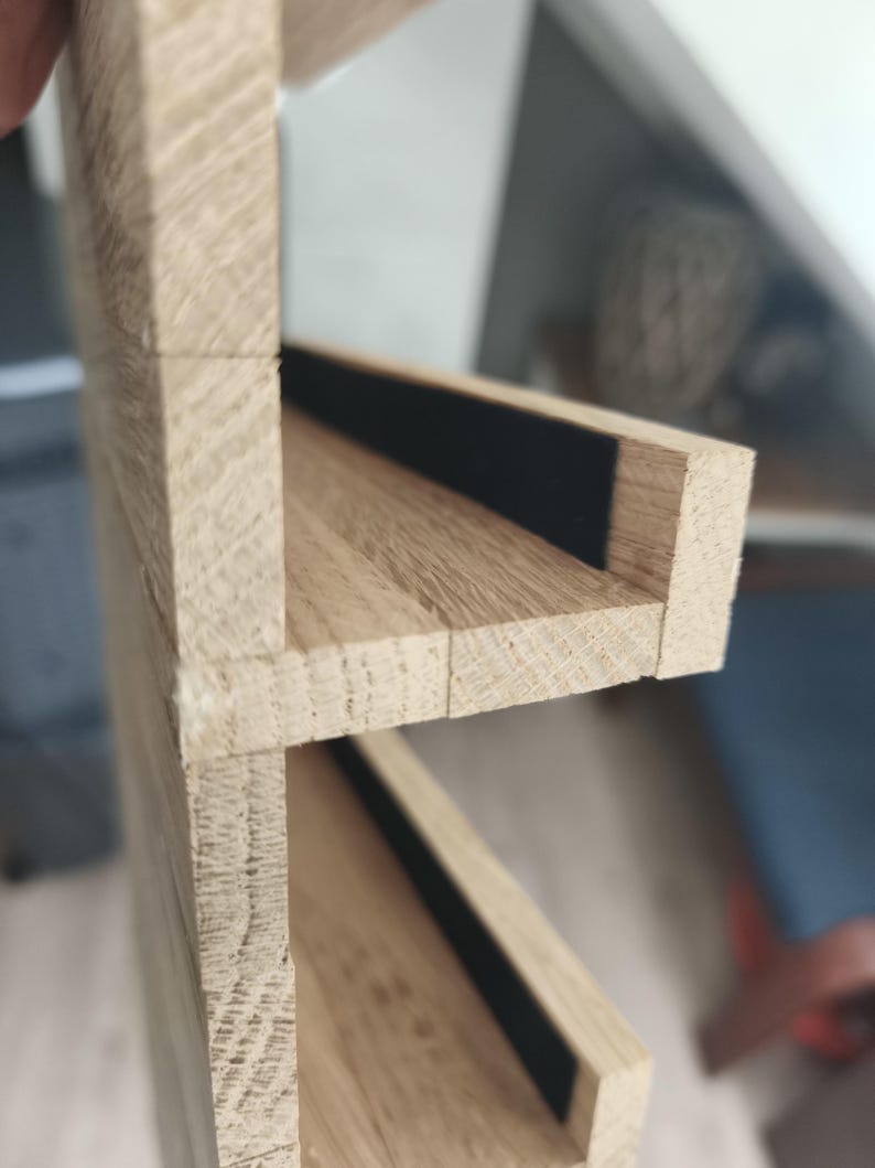 Puede incluir: Una estanter&iacute;a de madera de color claro con dos niveles horizontales y vetas visibles. Cada nivel de estante incluye una tira negra estrecha y empotrada a lo largo del borde posterior, que contrasta con el acabado de madera natural.