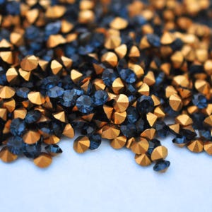 Peut inclure: Gros plan sur un tas de strass à facettes. Les strass sont un mélange de couleurs bleu foncé et or. Les strass dorés ont une finition métallique, tandis que les bleus sont plus translucides.