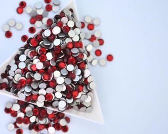 May include: A white triangular dish filled with red and silver round rhinestones. The rhinestones are scattered around the dish.
