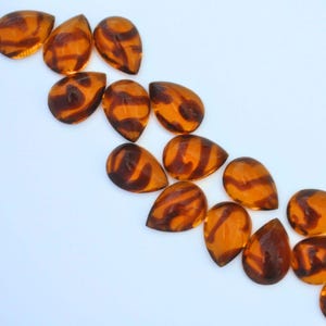May include: A collection of amber-colored glass teardrop-shaped beads with a brown swirl pattern.