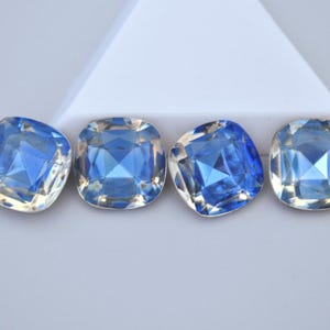 May include: Four square-cut, faceted gemstones with a vibrant blue hue. The gems have a cushion shape and are arranged in a row against a white background. The facets catch the light, creating a sparkling effect.