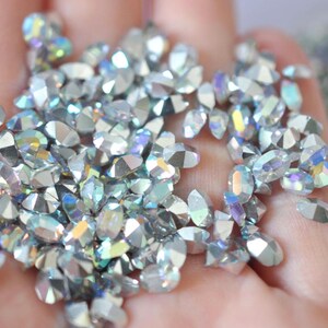 Peut inclure: Un ensemble de strass irisés et facettés. Les strass sont principalement argentés avec des éclats de couleurs arc-en-ciel. Les formes varient, incluant des ovales et des gouttes. Ces pierres précieuses décoratives conviennent aux travaux manuels et aux embellissements.