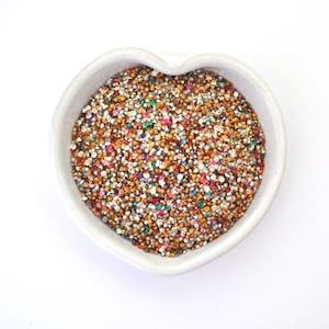 May include: A white heart-shaped bowl filled with a variety of colourful and metallic rhinestones.